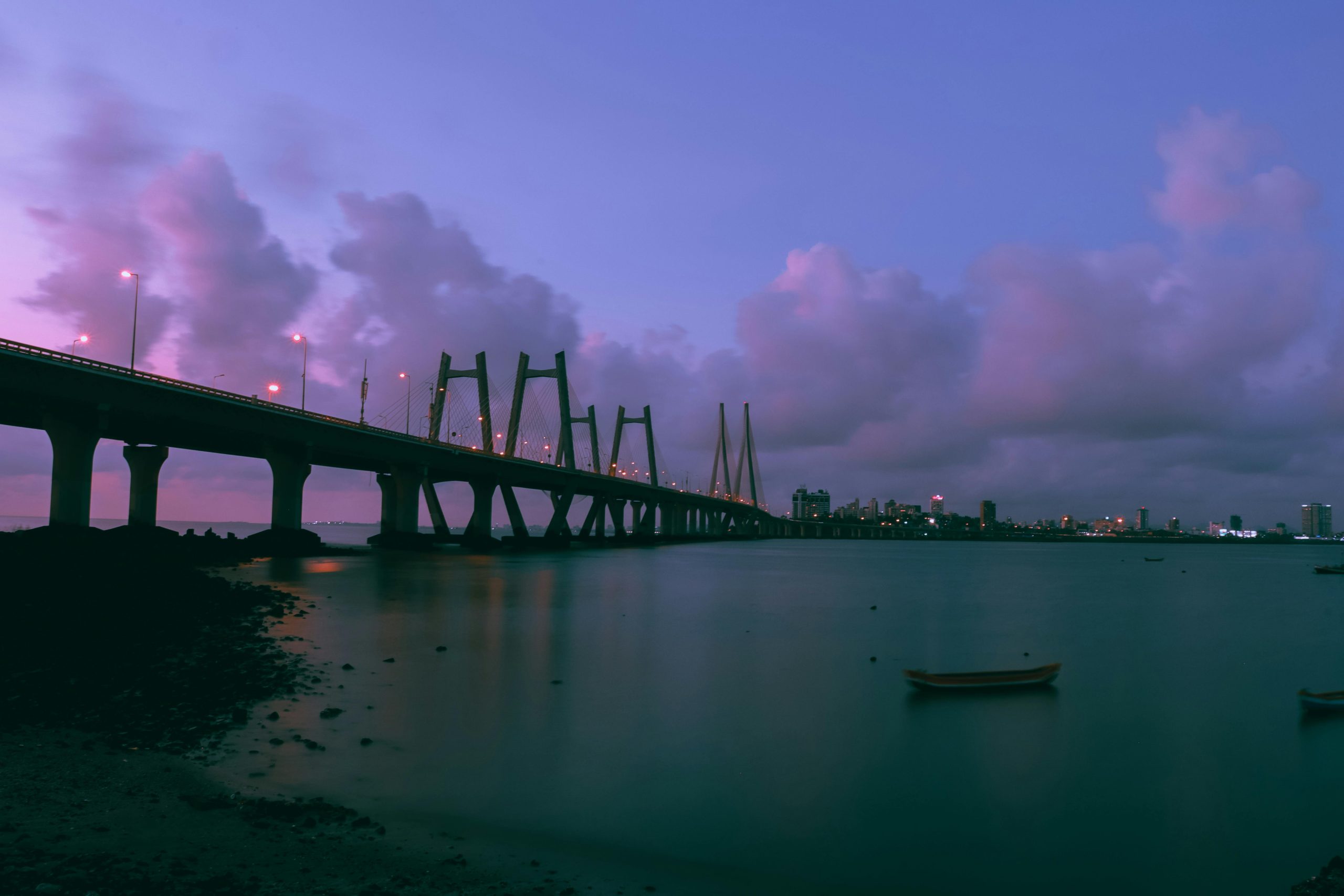 A stunning twilight photograph of an architectural bridge over calm waters, with a vibrant city skyline visible in the background.